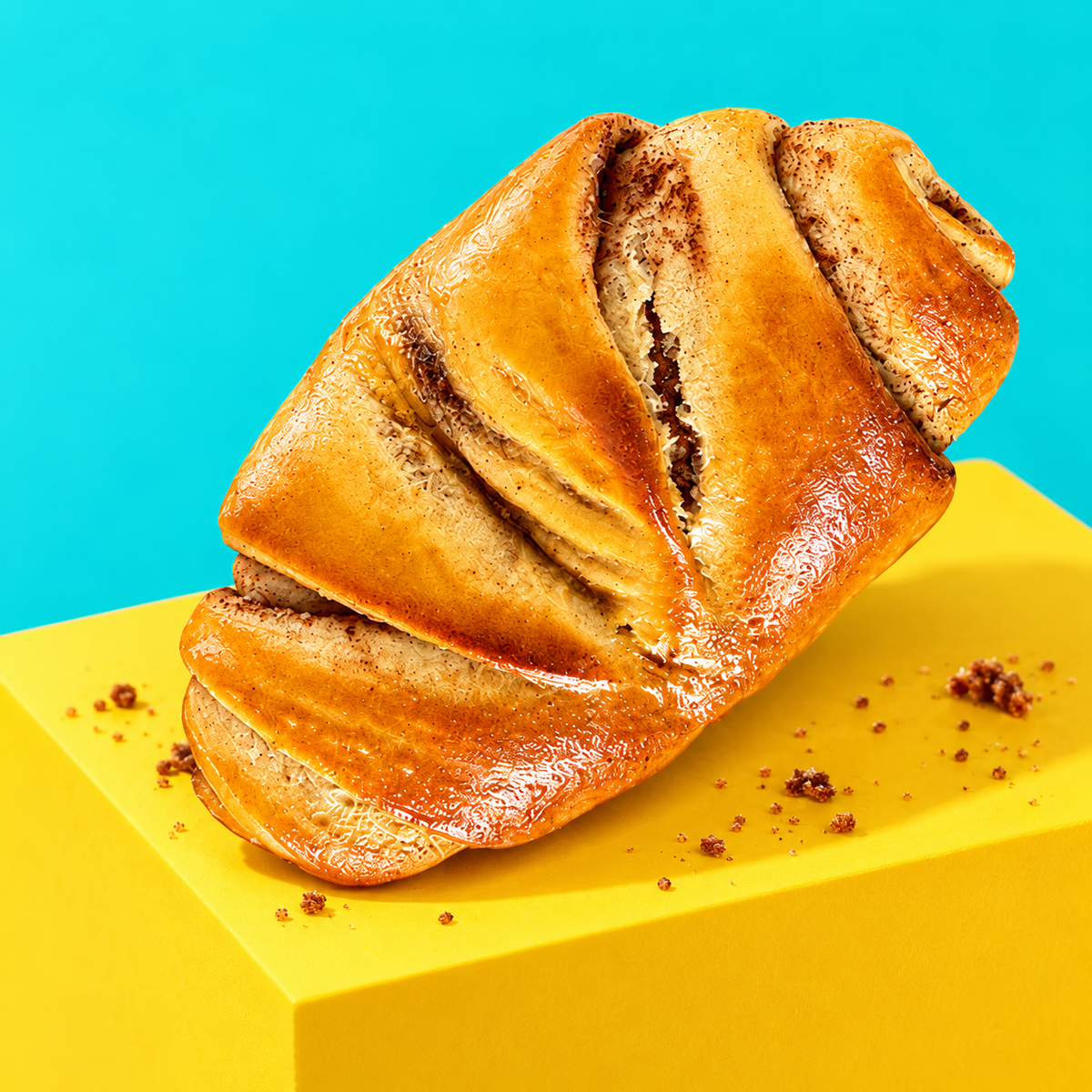 Goldenes Franzbrötchen auf einem gelben Podest vor Türkis
